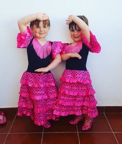 Portrait of smiling sisters wearing costume posing while standing against white wall