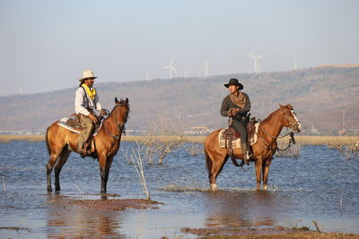 Men riding horses in lake against sky