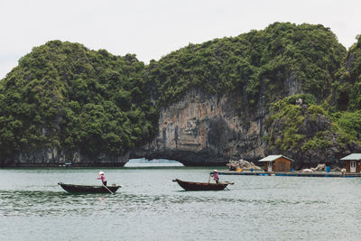 People sailing boats on river by rock formation against sky