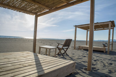 Wooden gazebo with chairs and table at beach against sky