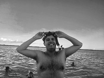 Smiling shirtless man holding snorkel in sea against sky