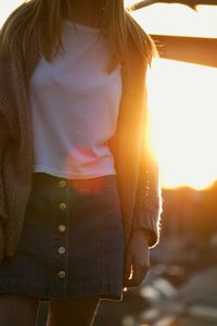 Midsection of young woman standing outdoors during sunset