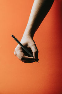Cropped hand of woman holding pen against colored background