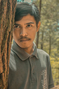 Portrait of young man standing against tree trunk