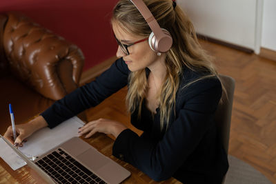 Woman working at home with laptop and papers on desk and headphones. home office . gray notebook 