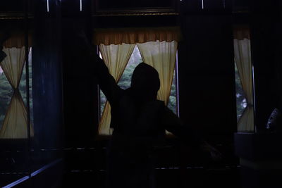 Rear view of silhouette woman standing by window at home