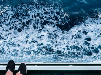 Low section of person standing on edge over sea