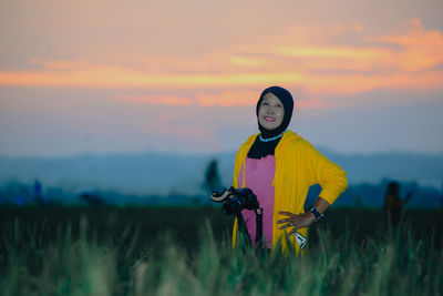 Portrait of young woman standing against sky during sunset