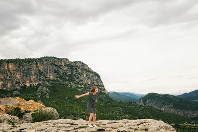 Playful young woman standing on rock against cloudy sky