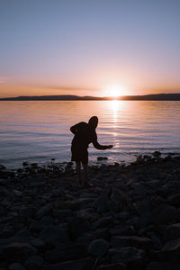 Man standing on rock at lakeshore against sky during sunset