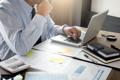 Midsection of businessman using laptop while sitting at desk