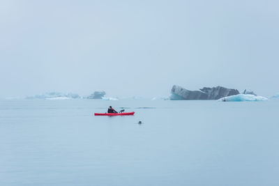 Man paddling in a kayak in the freezing waters of jokulsarlon glacier lagoon between icebergs
