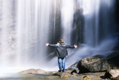 Full length of man standing by waterfall in forest