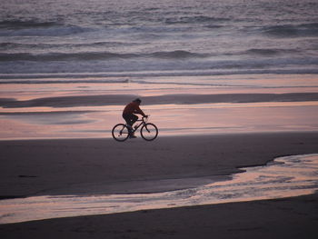 Side view of man riding bicycle at beach during sunset