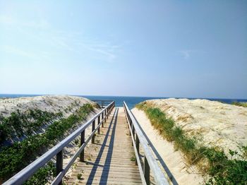 Boardwalk leading towards sea against sky