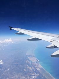 Aerial view of airplane wing over landscape against blue sky