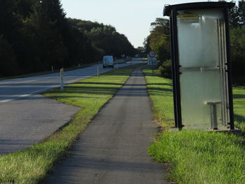 Empty road amidst trees on field against sky
