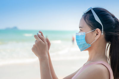 Woman wearing mask photographing sea against clear sky