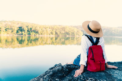 Rear view of woman sitting by lake against clear sky