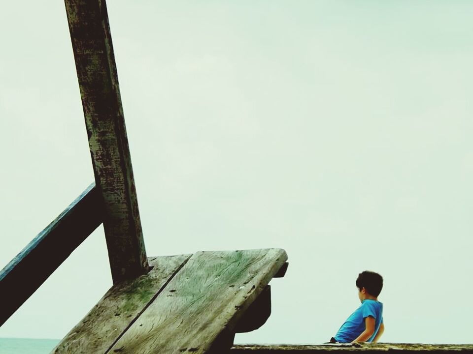 clear sky, leisure activity, lifestyles, sky, childhood, copy space, rear view, sitting, beach, sea, railing, day, men, blue, casual clothing, low angle view, nature, boys