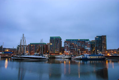 Sailboats moored on river by buildings in city against sky