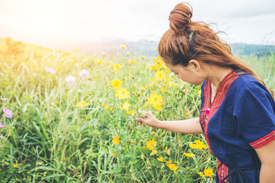 Side view of woman touching flowering plant at field