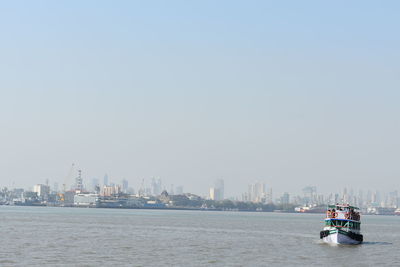 Nautical vessel on sea by buildings against clear sky