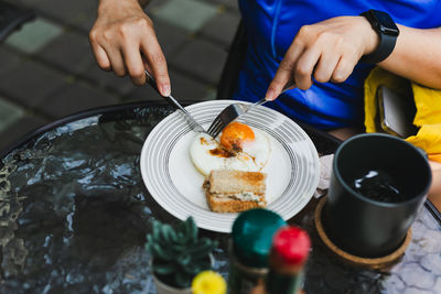 Women eating fried egg with fork and knife at restaurant.
