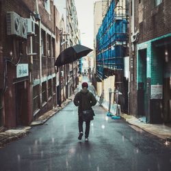 Rear view of man walking on street with umbrella in air