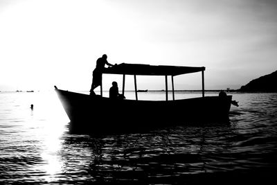 Silhouette man standing on fishing boat in sea against sky