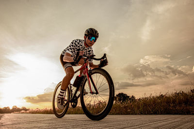 Man riding bicycle on street against sky during sunset