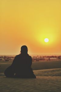 Silhouette woman sitting on desert at sunset