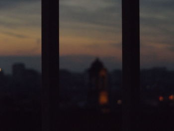 Silhouette built structure against sunset sky seen through window