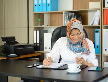 Young woman using mobile phone while sitting on table