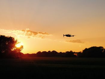 Airplane flying over field against sky during sunset