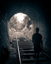 Rear view of silhouette man standing on railroad tracks in tunnel