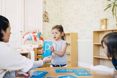 Teacher looking at girl holding letter p in classroom