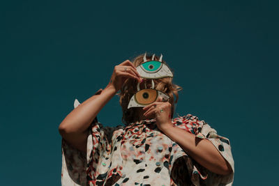 Woman with make-up holding cardboard decoration against clear sky