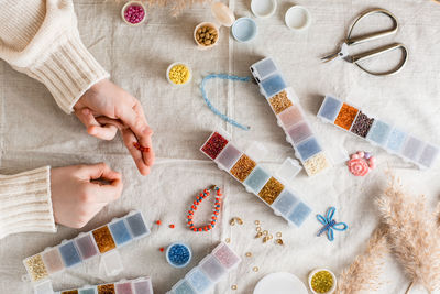 The girl's hands are weaving a beaded bracelet and items for beading on the table. 