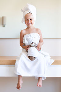 Little girl in a white bath towel and a turban sits, smiles, holds a teddy bear. family look.