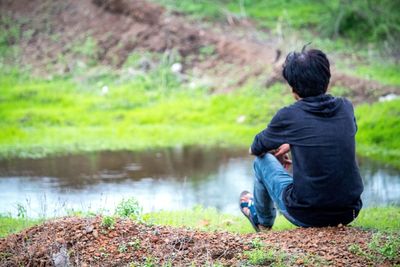 Rear view of man sitting at lakeshore