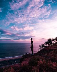 Man standing on shore against sky during sunset