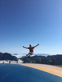 Woman jumping on mountain against clear blue sky