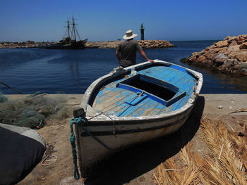Rear view of man leaning on moored rowboat at beach against sky