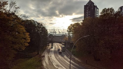 Road by trees in city against sky