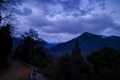 Road amidst trees and mountains against sky