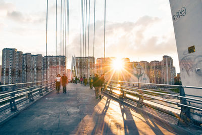 People on bridge in city against sky during sunset