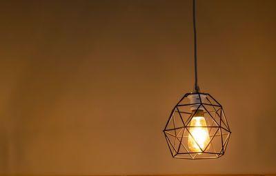 Low angle view of illuminated light bulb hanging against wall
