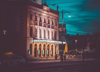 Illuminated street by buildings in city at night