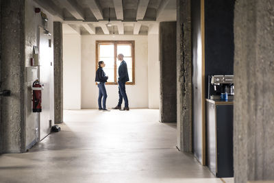 Business people talking while standing by window at office